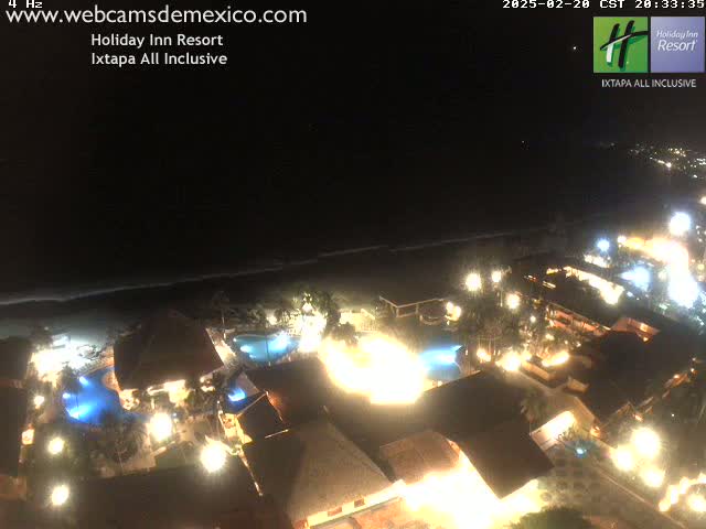 A brightly lit resort at night, situated near a dark ocean under a clear, night sky.