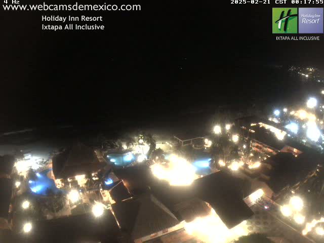 A brightly lit resort at night, next to a dark ocean under a clear, dark sky.