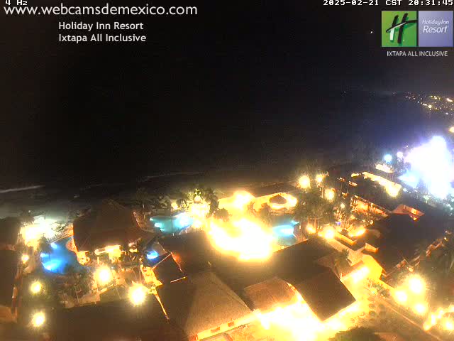 A brightly lit resort at night, situated on a beach under a dark sky.