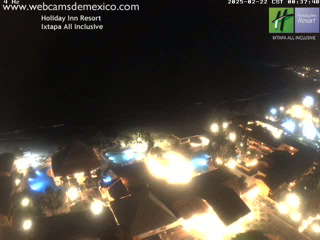 A brightly lit resort at night, situated on a beach next to a dark ocean under a clear, dark sky.
