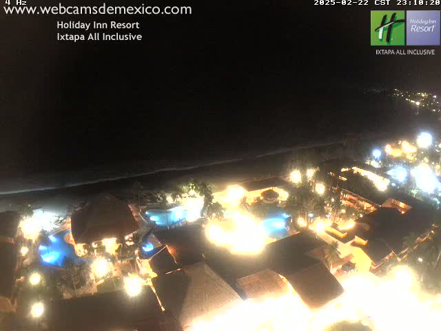 A brightly lit resort at night, next to a dark ocean under a clear sky.