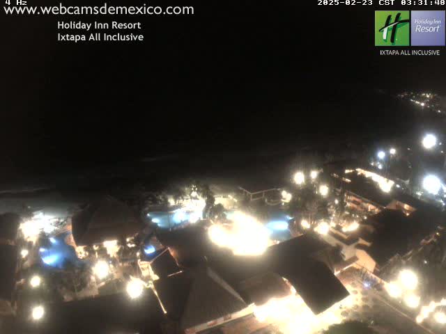 A brightly lit resort at night, next to a dark beach under a clear sky.