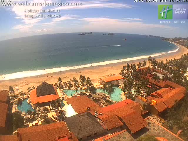 An aerial view of a resort on a beach with calm ocean water under a mostly sunny sky.