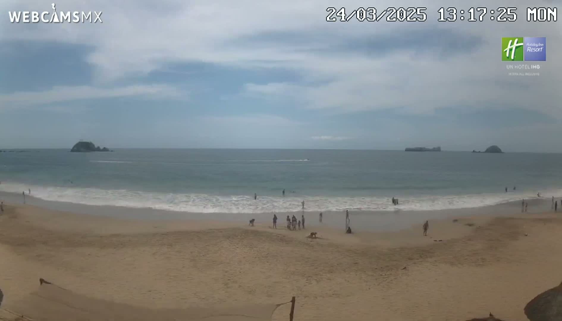 A sandy beach with small waves and scattered people under a partly cloudy sky.
