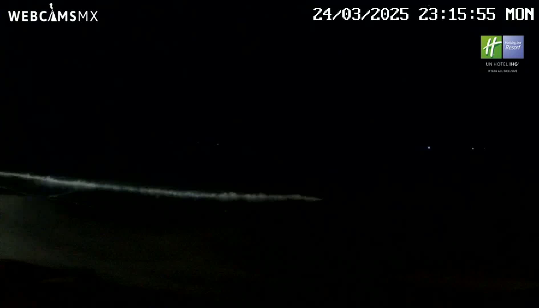 A nighttime view of an ocean with waves gently breaking on the shore under a dark, clear sky.