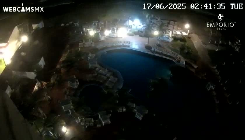 An aerial nighttime view of a resort pool area with surrounding buildings and landscaping.