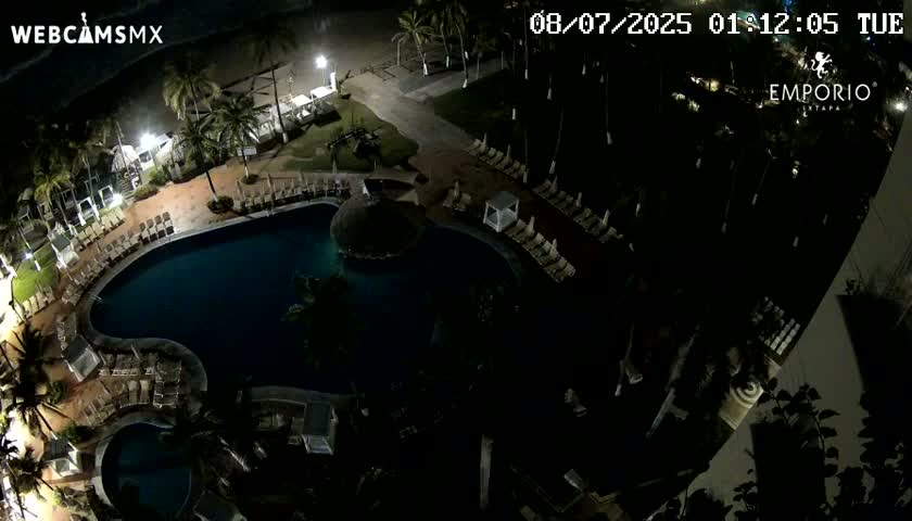 A nighttime aerial view shows a resort pool area with surrounding lounge chairs and palm trees.