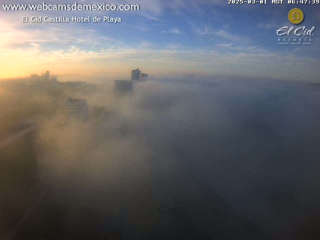 A city skyline is partially obscured by a thick layer of fog at sunrise.