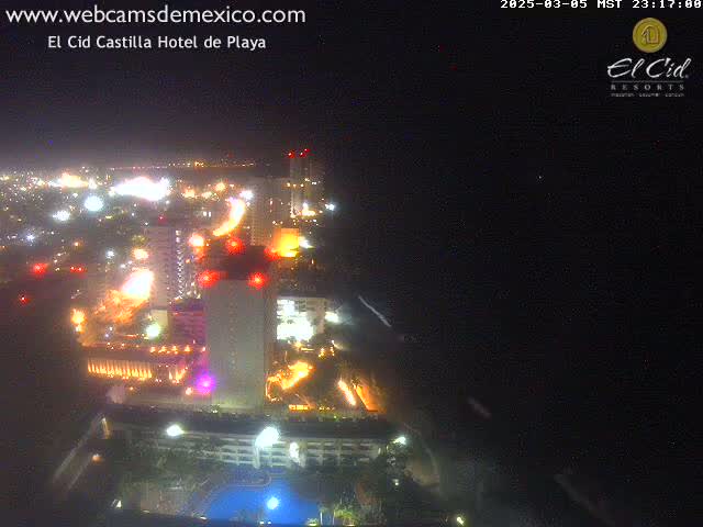 A nighttime aerial view of a brightly lit resort complex near a coastline under a clear, dark sky.