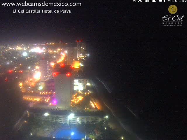 A nighttime aerial view of a brightly lit coastal resort town with a dark ocean.