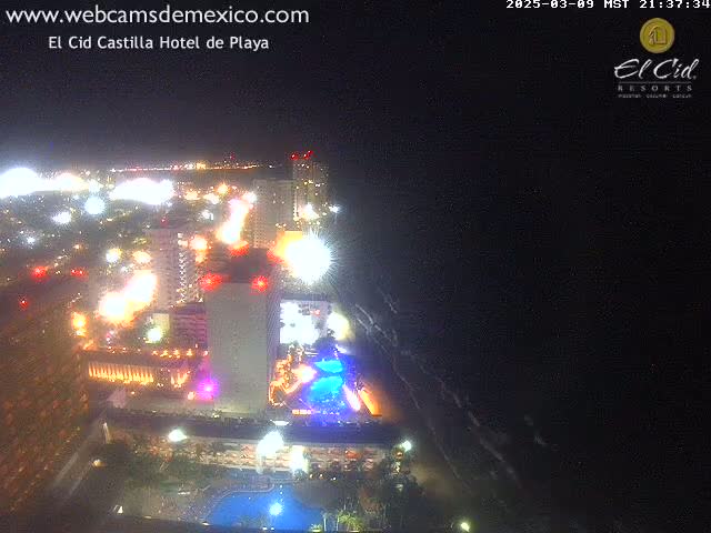 A brightly lit beachfront hotel and surrounding city at night, viewed from above under a dark, clear sky.