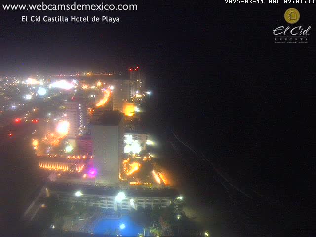 A brightly lit coastal city at night, with a dark ocean visible in the foreground under a clear sky.
