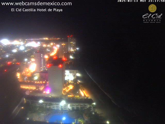 A nighttime aerial view of a brightly lit coastal city with a dark ocean and a beach.