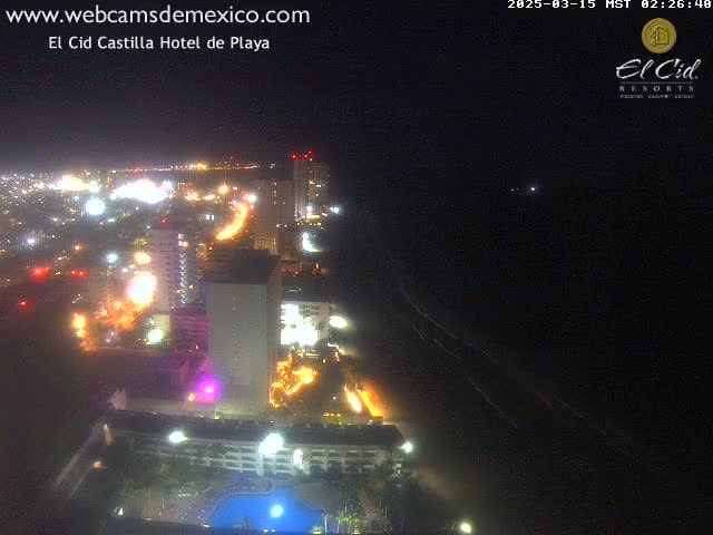 A nighttime, aerial view of a brightly lit coastal city with a dark ocean and beach.