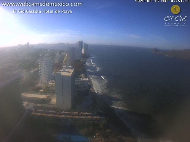 A hazy, sunny day overlooking a coastal city with high-rise buildings and a beach with waves lapping the shore.