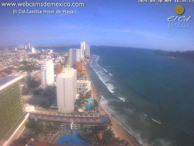 A beach with gentle waves laps a sandy shore lined with high-rise hotels under a clear blue sky.