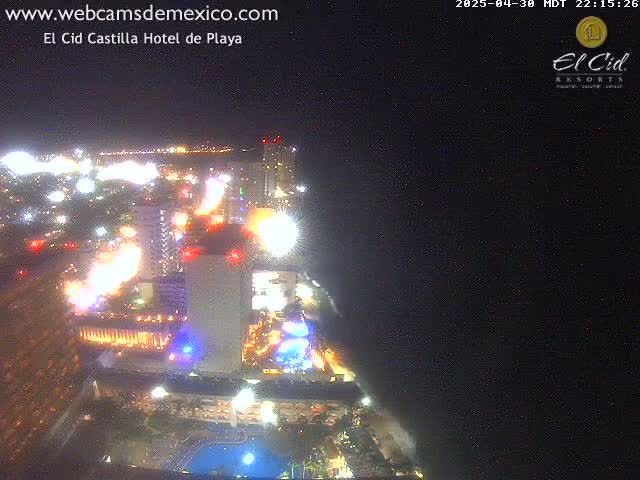 A brightly lit hotel complex at night overlooks a dark ocean under a clear sky.