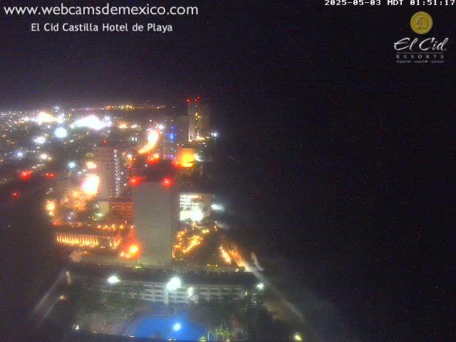 A brightly lit coastal city at night is seen from above, next to a dark ocean under a clear sky.