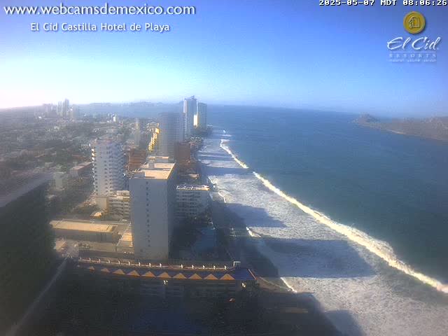 A coastal city with high-rise buildings and a sandy beach with waves rolling in under a clear blue sky.