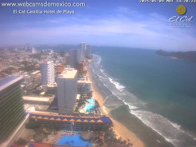 An aerial view shows a beach with gentle waves under a mostly sunny sky, next to a city with high-rise hotels and buildings.