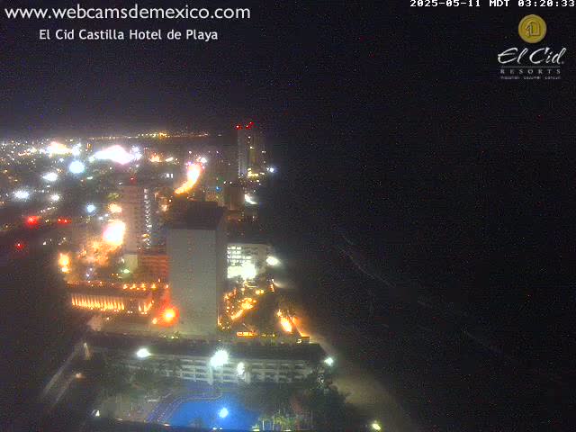 A nighttime, aerial view of a brightly lit coastal city with a dark ocean in the background.