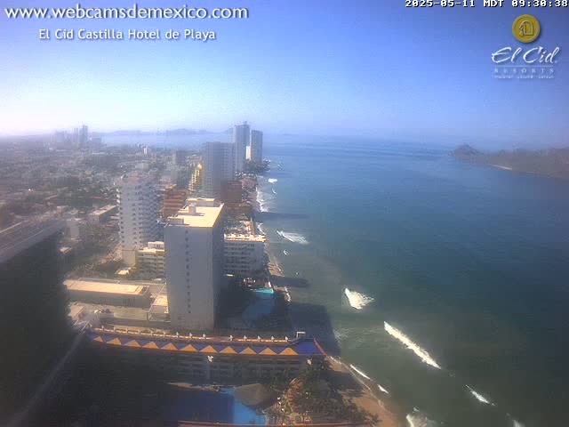 A coastal city with high-rise hotels and buildings stretches along a sandy beach next to a calm ocean under a clear sky.