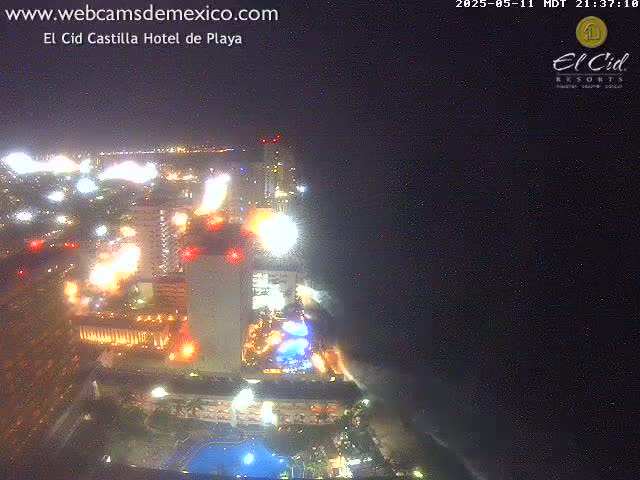 A brightly lit resort hotel at night, overlooking a dark ocean under a clear sky.
