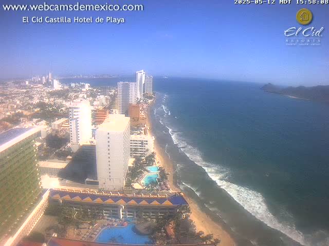 A sunny coastal city with high-rise hotels and a sandy beach bordered by ocean waves.