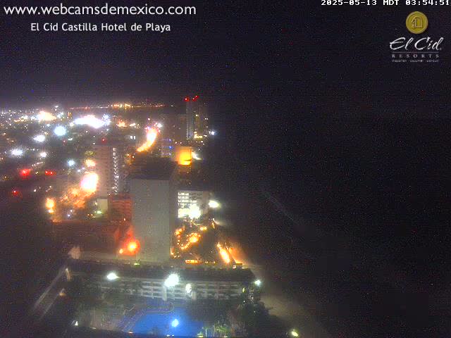 A nighttime aerial view of a brightly lit coastal city with a dark ocean in the background.