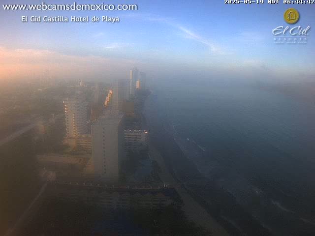 A hazy, sunrise view shows a coastal city with numerous high-rise buildings and a dark-colored ocean.