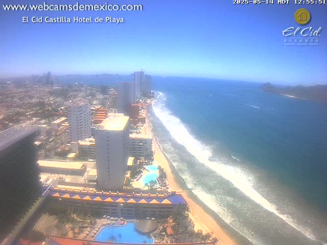 A beach with ocean waves stretches alongside a coastal city under a clear blue sky.