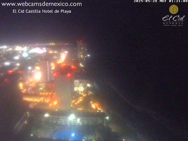An aerial nighttime view of a brightly lit coastal city with a dark ocean in the background under a clear sky.