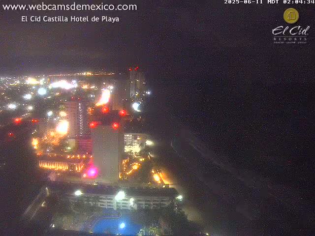 A brightly lit hotel complex at night, situated near a coastline under a dark, clear sky.
