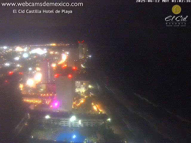A brightly lit resort complex at night is situated next to a dark ocean under a clear sky.