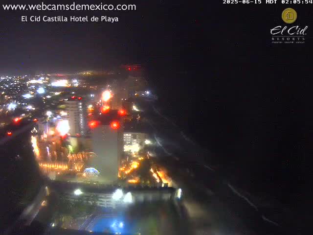 A nighttime aerial view of a brightly lit beachfront city with ocean waves visible in the dark water.