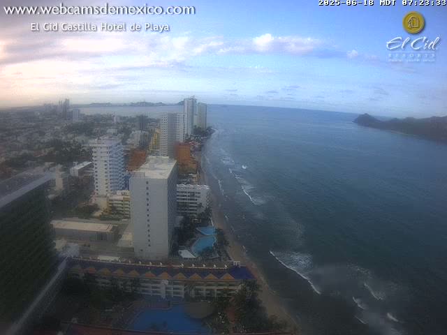 An aerial view shows a coastal city with high-rise buildings and a beach under a partly cloudy sky.