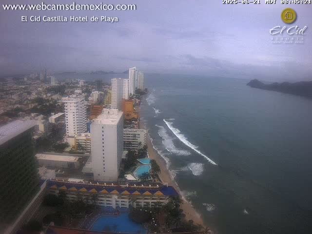 An overcast coastal city scene shows a beach with waves, hotels, and high-rise buildings.