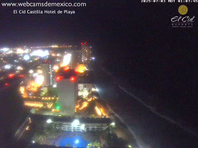 A brightly lit beachfront resort at night, with a clear, dark sky and calm ocean.