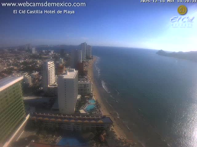 A vibrant nighttime aerial view captures a brightly lit city with numerous buildings and a hotel pool sprawling along a dark coastline, with the ocean visible under a clear sky.