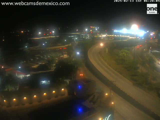 An elevated nighttime view of a highway interchange with sparse traffic, surrounded by dimly lit buildings and vegetation.