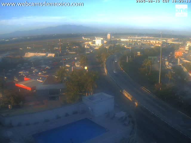An elevated view of an airport and surrounding area at sunrise, showing a highway curving through a landscape of buildings, parking lots, and vegetation.