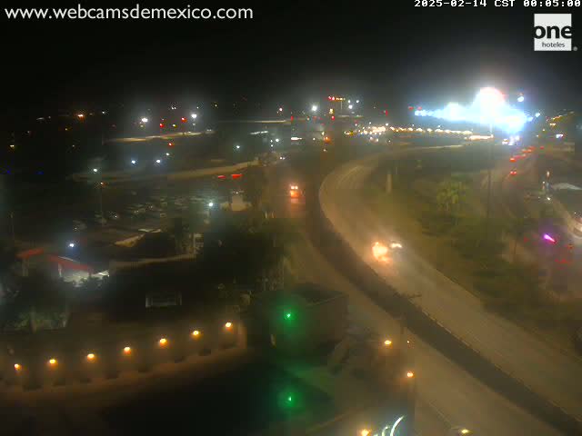 A nighttime, aerial view of a highway interchange with several vehicles traveling on the roads, surrounded by buildings and some vegetation.