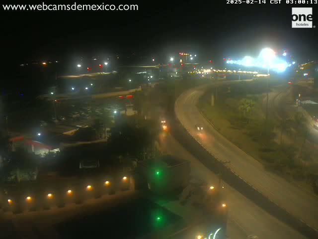A nighttime, high-angle view of a highway interchange with several vehicles driving on it, surrounded by buildings and vegetation.