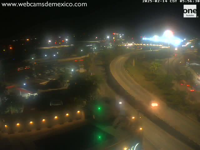 A nighttime aerial view of a highway curving through a city, with sparsely populated areas and buildings visible, under clear skies.