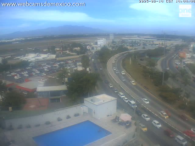 An outdoor, hazy view shows a highway curving past an airport with parked planes, a parking lot full of cars, and a swimming pool at a building complex.