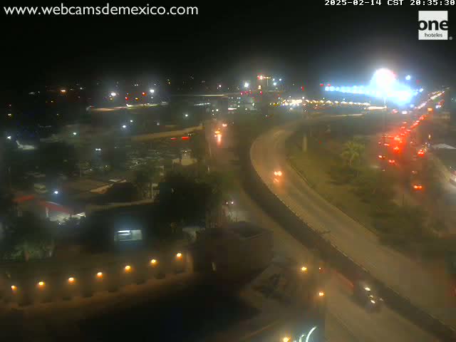 A nighttime, high-angle view of a highway curving around an airport with planes on the tarmac and traffic lights visible.