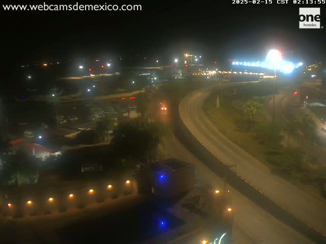 A nighttime, overhead view of a highway curving through a parking lot and other structures, with some vehicle traffic visible.