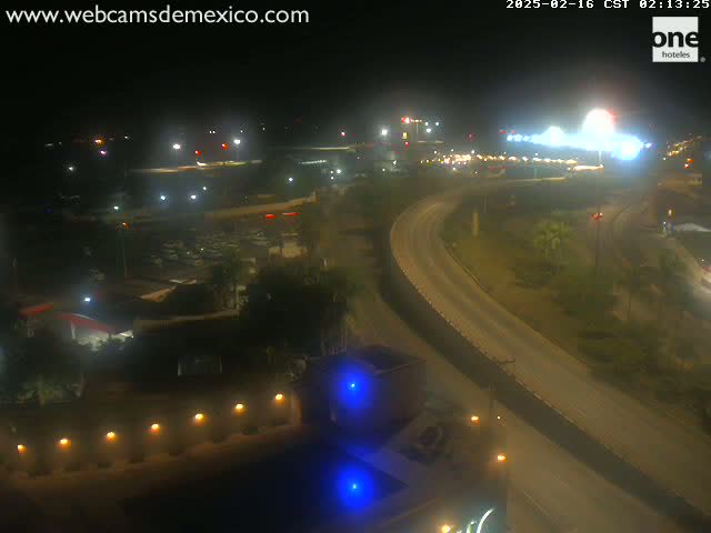 A nighttime, high-angle view of a highway curving through a landscape dotted with buildings and vegetation.