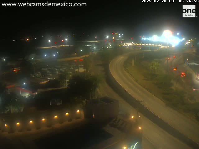A nighttime, high-angle view shows a highway curving through a sparsely lit landscape with some buildings and vegetation.