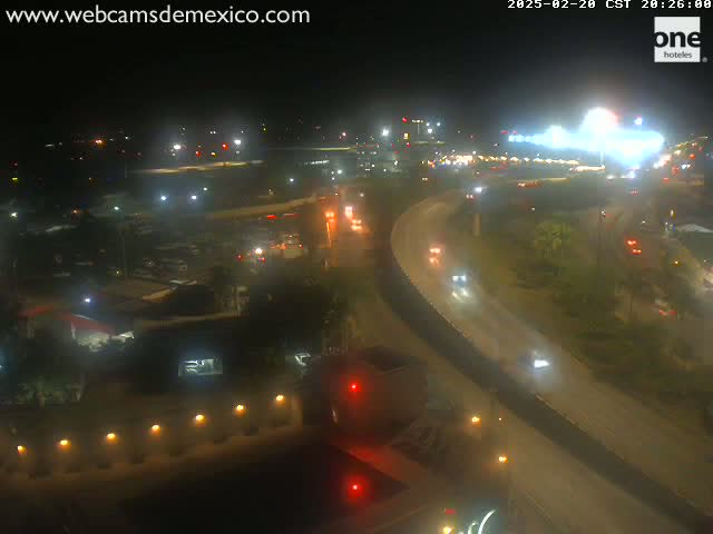 A nighttime, high-angle view of a highway interchange with sparse traffic, surrounded by dimly lit buildings and vegetation.